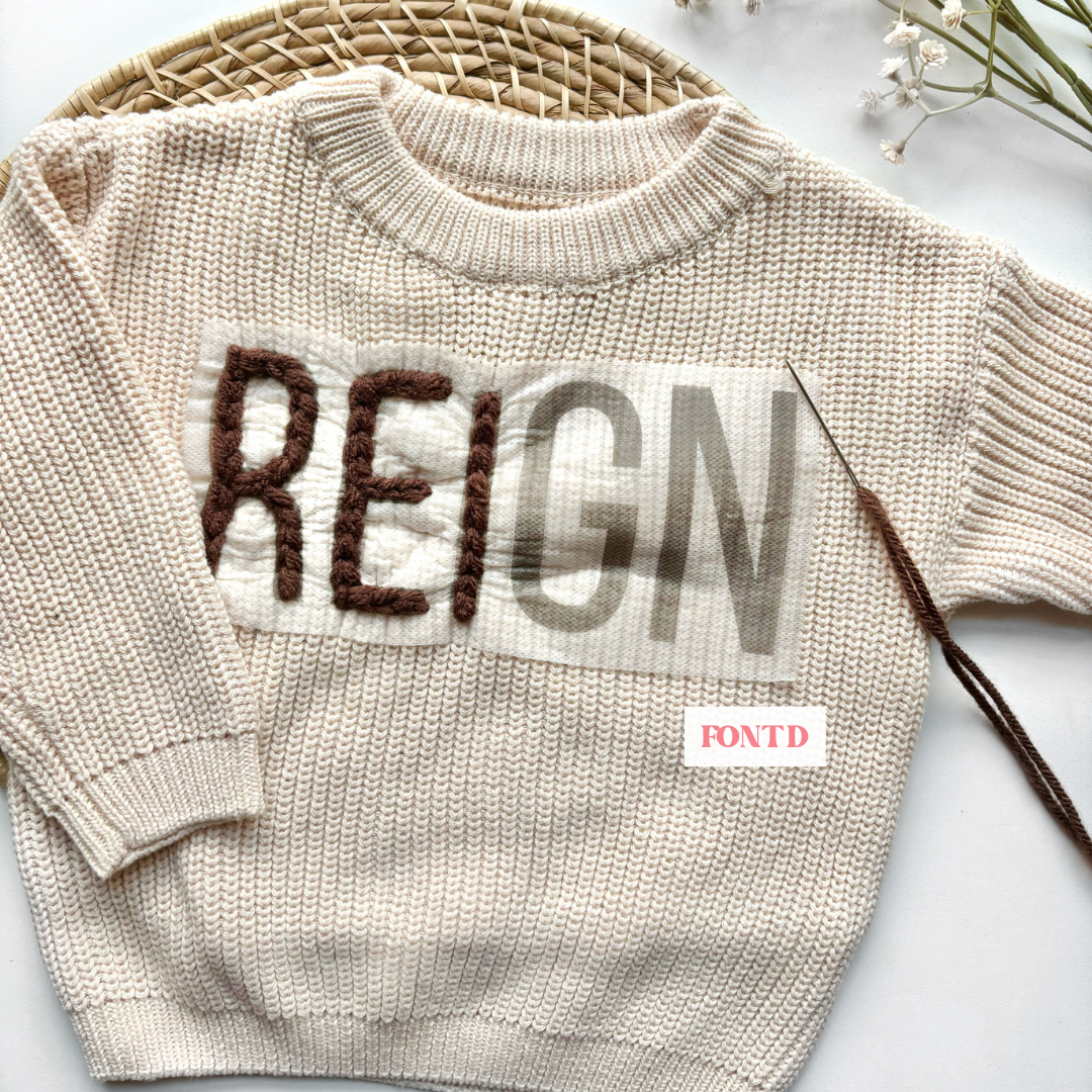 Baby boy neutral knit sweater with brown yarn and a stick and stitch name pattern